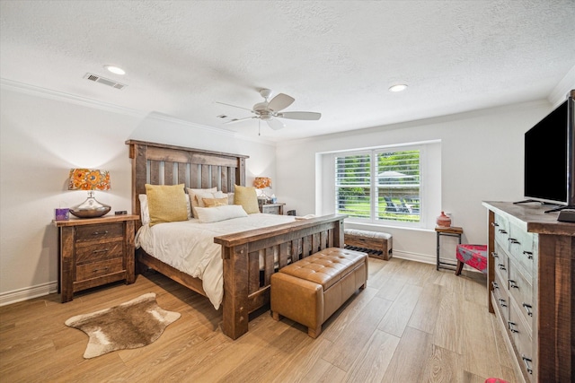 bedroom with light wood finished floors, visible vents, a textured ceiling, and ornamental molding
