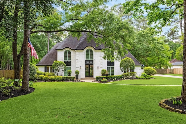 french provincial home with french doors, fence, a front yard, brick siding, and roof with shingles