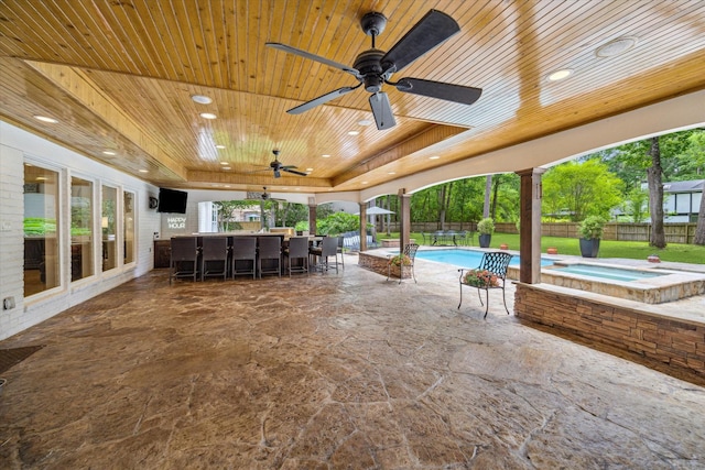 view of patio / terrace with ceiling fan, a fenced backyard, outdoor dry bar, and a pool with connected hot tub