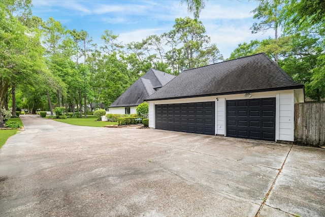 view of side of property with fence, a shingled roof, and a garage