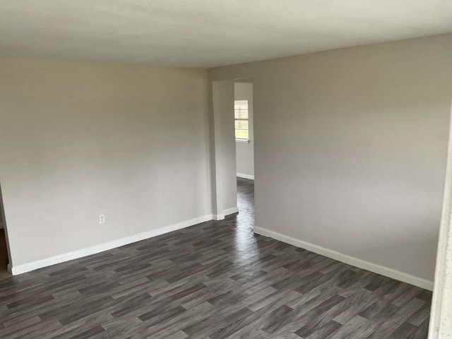 spare room featuring baseboards and dark wood-style floors
