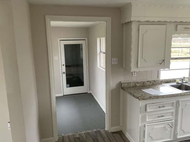 kitchen with light countertops, baseboards, a sink, and white cabinetry