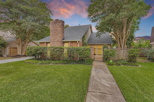 tudor-style house featuring roof with shingles, fence, and a front lawn