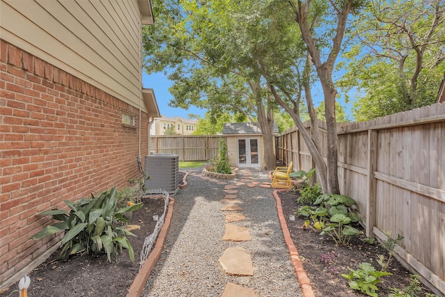 view of yard with central AC unit, french doors, a fenced backyard, and an outbuilding