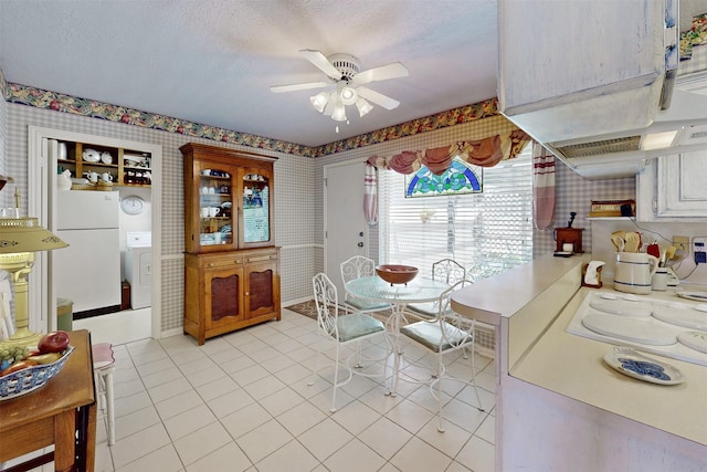 dining area featuring a textured ceiling, wallpapered walls, light tile patterned floors, ceiling fan, and washer / clothes dryer