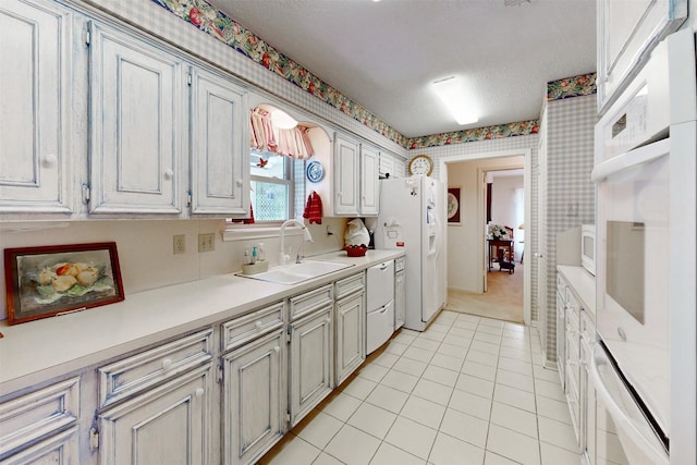 kitchen featuring wallpapered walls, light countertops, white appliances, light tile patterned floors, and a sink