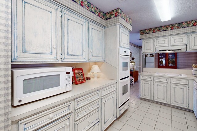 kitchen featuring wallpapered walls, light countertops, white appliances, and light tile patterned floors