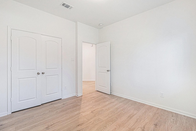 unfurnished bedroom featuring baseboards, light wood-style flooring, visible vents, and a closet