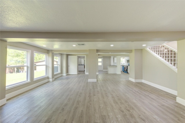 unfurnished living room with recessed lighting, visible vents, light wood-type flooring, baseboards, and stairs