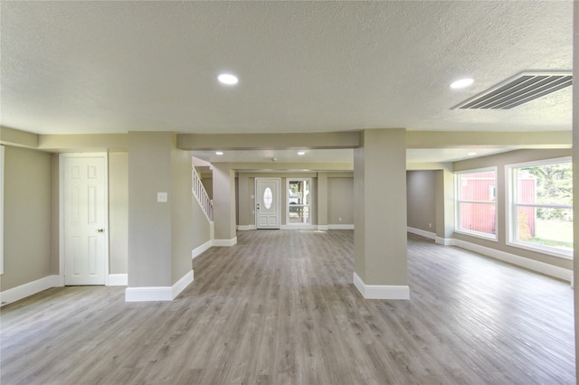 unfurnished living room with baseboards, a textured ceiling, visible vents, and light wood-style flooring
