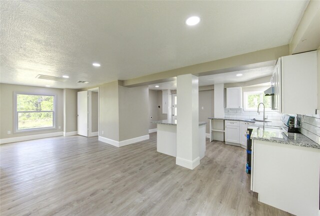 kitchen featuring light wood finished floors, light stone countertops, tasteful backsplash, open floor plan, and white cabinetry