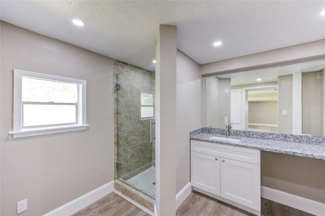 bathroom featuring wood finished floors, plenty of natural light, a stall shower, vanity, and baseboards