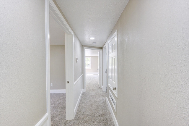 corridor featuring carpet floors, a textured ceiling, baseboards, and a textured wall