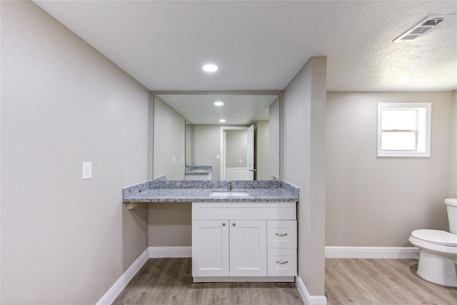 half bath featuring baseboards, wood finished floors, visible vents, and toilet