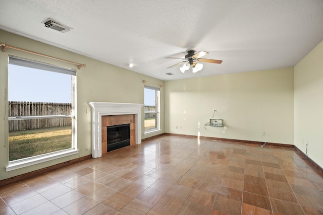 unfurnished living room featuring visible vents, a ceiling fan, baseboards, a tiled fireplace, and a textured ceiling