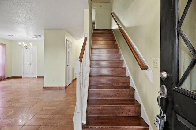 stairway with a textured ceiling, tile patterned floors, baseboards, and a notable chandelier