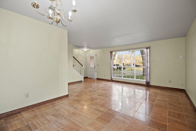 tiled empty room with a chandelier, stairway, a textured ceiling, and baseboards