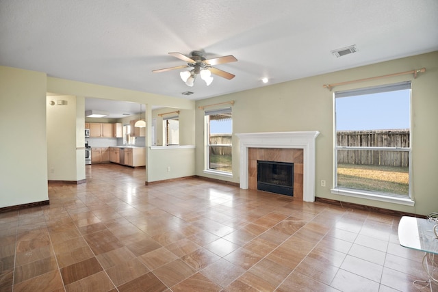 unfurnished living room featuring a ceiling fan, light tile patterned floors, a tile fireplace, baseboards, and visible vents