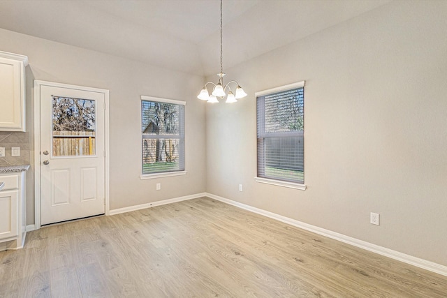 unfurnished dining area featuring light wood-style floors, vaulted ceiling, baseboards, and an inviting chandelier