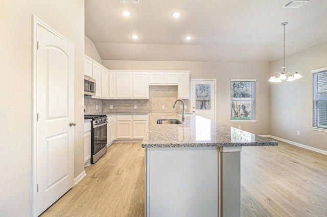 kitchen featuring stainless steel appliances, light wood-style flooring, a sink, decorative backsplash, and light stone countertops