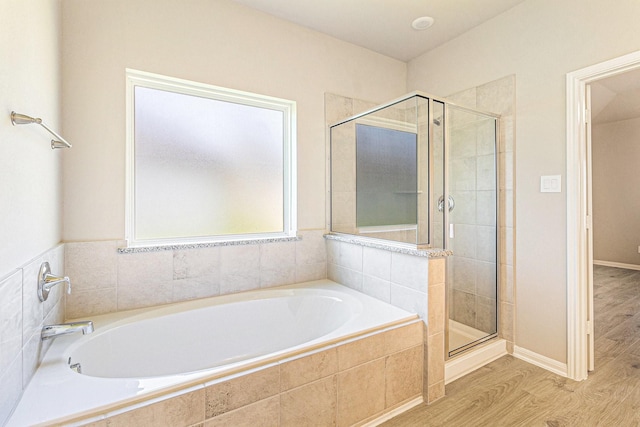 bathroom featuring a bath, a shower stall, baseboards, and wood finished floors