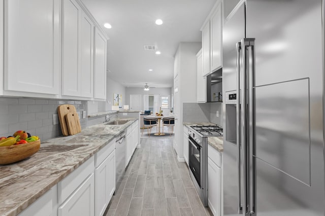 24709 Stablewood Forest Ct, Huffman, TX 77336 - kitchen featuring stainless steel appliances, white cabinets, a sink, recessed lighting, and light stone countertops
