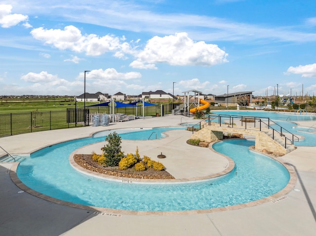 pool with a water slide, playground community, fence, a water play area, and a patio area