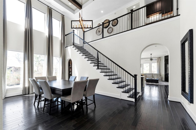 dining room featuring baseboards, a towering ceiling, arched walkways, and stairs