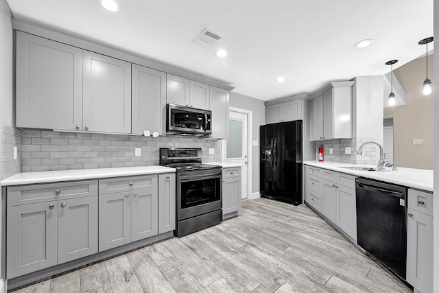 kitchen with light countertops, gray cabinets, a sink, decorative backsplash, and black appliances