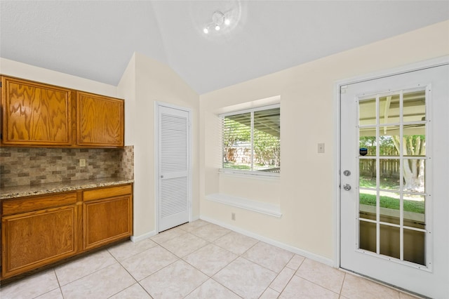 17402 Eastwood Cir, Houston, TX 77095 - kitchen featuring backsplash, lofted ceiling, brown cabinetry, light tile patterned floors, and light stone countertops