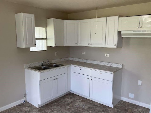 kitchen with baseboards, under cabinet range hood, a sink, and white cabinetry
