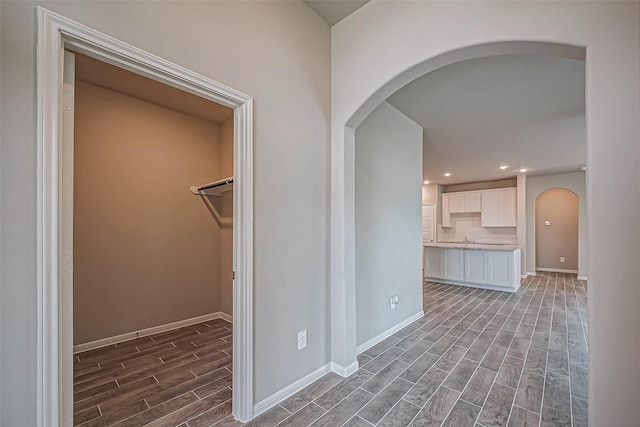 hall with recessed lighting, arched walkways, wood tiled floor, and baseboards