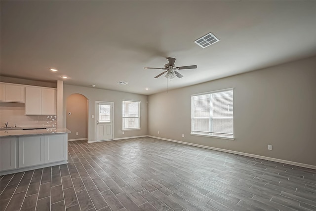 unfurnished living room with ceiling fan, arched walkways, baseboards, dark wood-style flooring, and visible vents