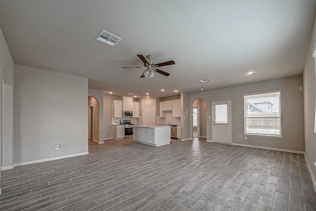 unfurnished living room with baseboards, visible vents, arched walkways, and ceiling fan