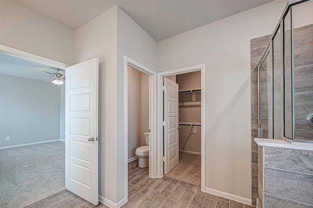bathroom featuring a walk in closet, wood finish floors, toilet, and a stall shower