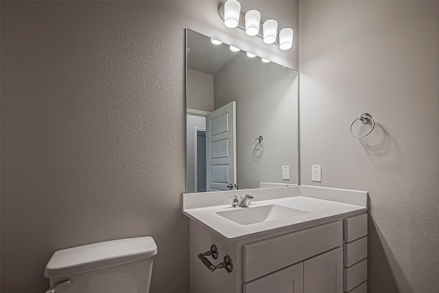 half bathroom featuring a textured wall, toilet, and vanity