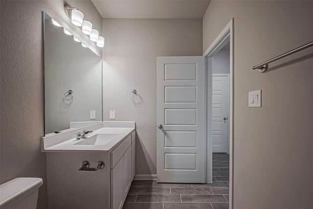 half bathroom with baseboards, vanity, and toilet