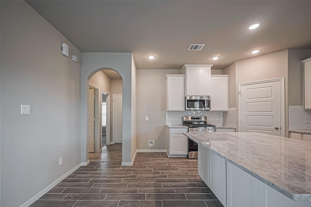 kitchen with white cabinets, arched walkways, baseboards, backsplash, and appliances with stainless steel finishes