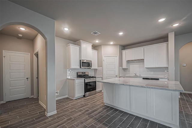 kitchen featuring wood tiled floor, stainless steel appliances, visible vents, arched walkways, and white cabinetry