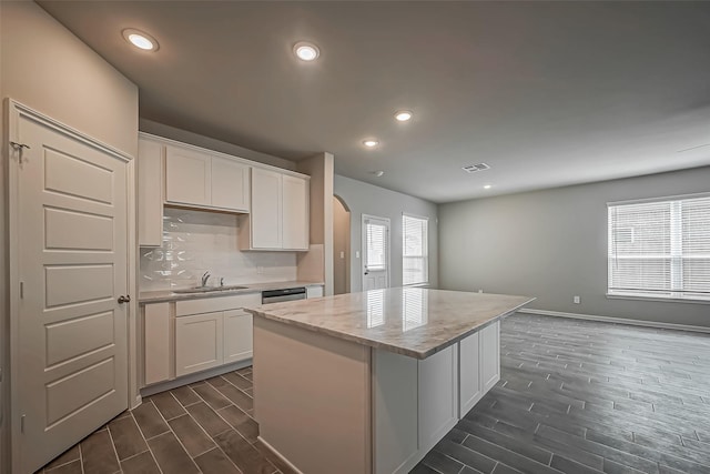 kitchen with a sink, dishwashing machine, arched walkways, wood finish floors, and visible vents