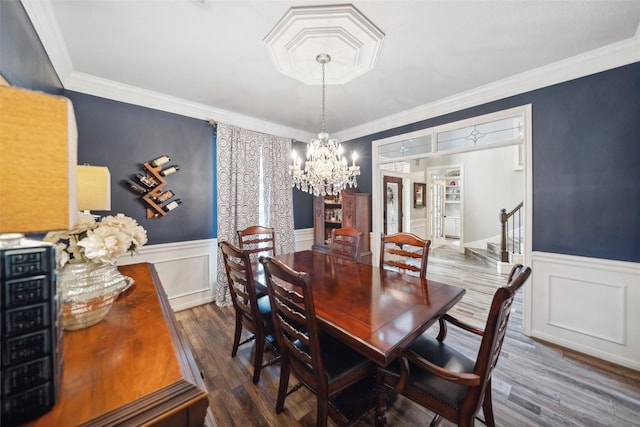 dining space featuring wood finished floors, ornamental molding, a decorative wall, wainscoting, and a notable chandelier