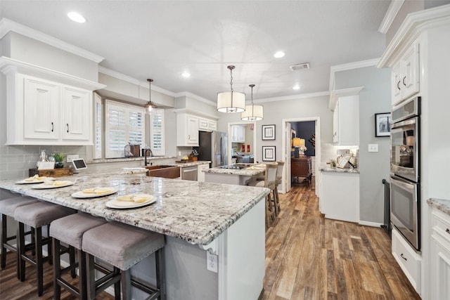 kitchen featuring visible vents, a sink, a center island, a peninsula, and appliances with stainless steel finishes