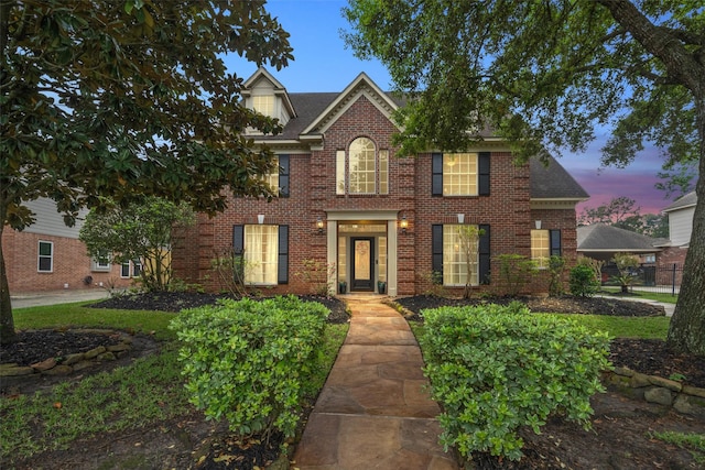 colonial inspired home featuring fence, brick siding, and roof with shingles