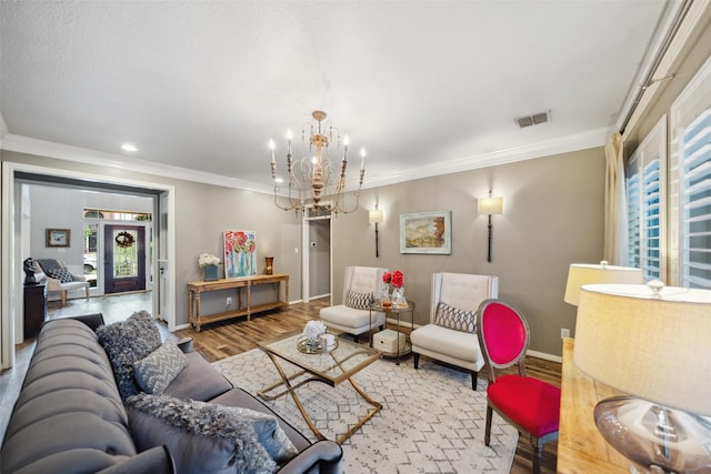 living area featuring wood finished floors, an inviting chandelier, baseboards, ornamental molding, and visible vents