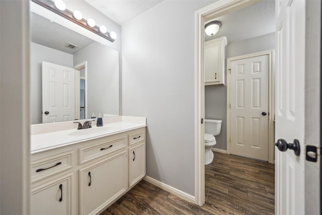 bathroom with toilet, visible vents, baseboards, wood finished floors, and vanity