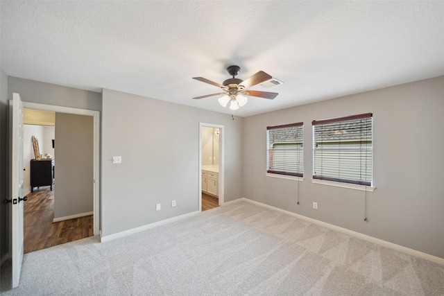 unfurnished bedroom featuring light carpet, ensuite bathroom, baseboards, visible vents, and ceiling fan