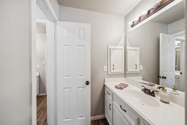 bathroom featuring baseboards, wood finished floors, a textured ceiling, and vanity