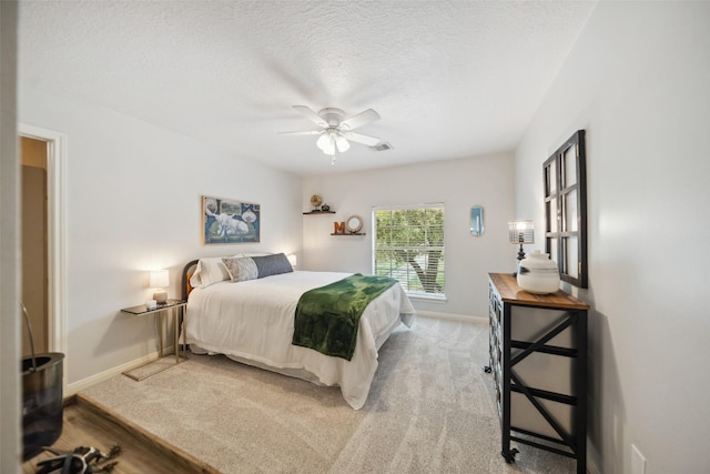 bedroom with a textured ceiling, baseboards, visible vents, light colored carpet, and ceiling fan