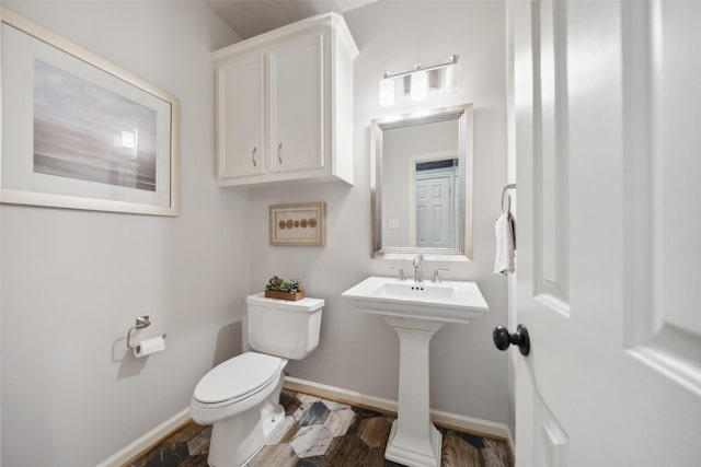 half bathroom featuring a sink, toilet, wood finished floors, and baseboards
