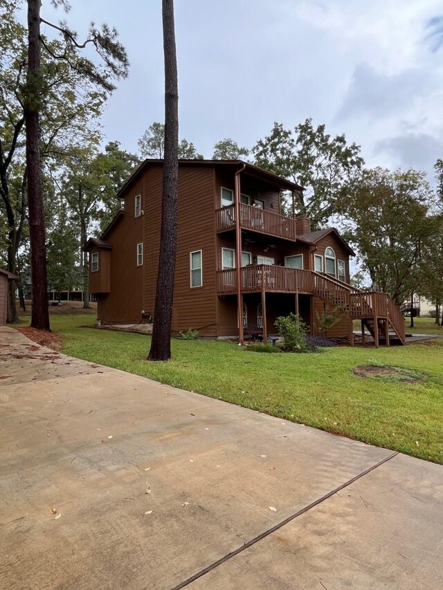 rear view of property featuring stairway, a wooden deck, a balcony, and a yard